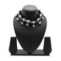 Handmade black crochet choker necklace featuring white cowrie shells and hanging silver bohemian coins on a black display stand.