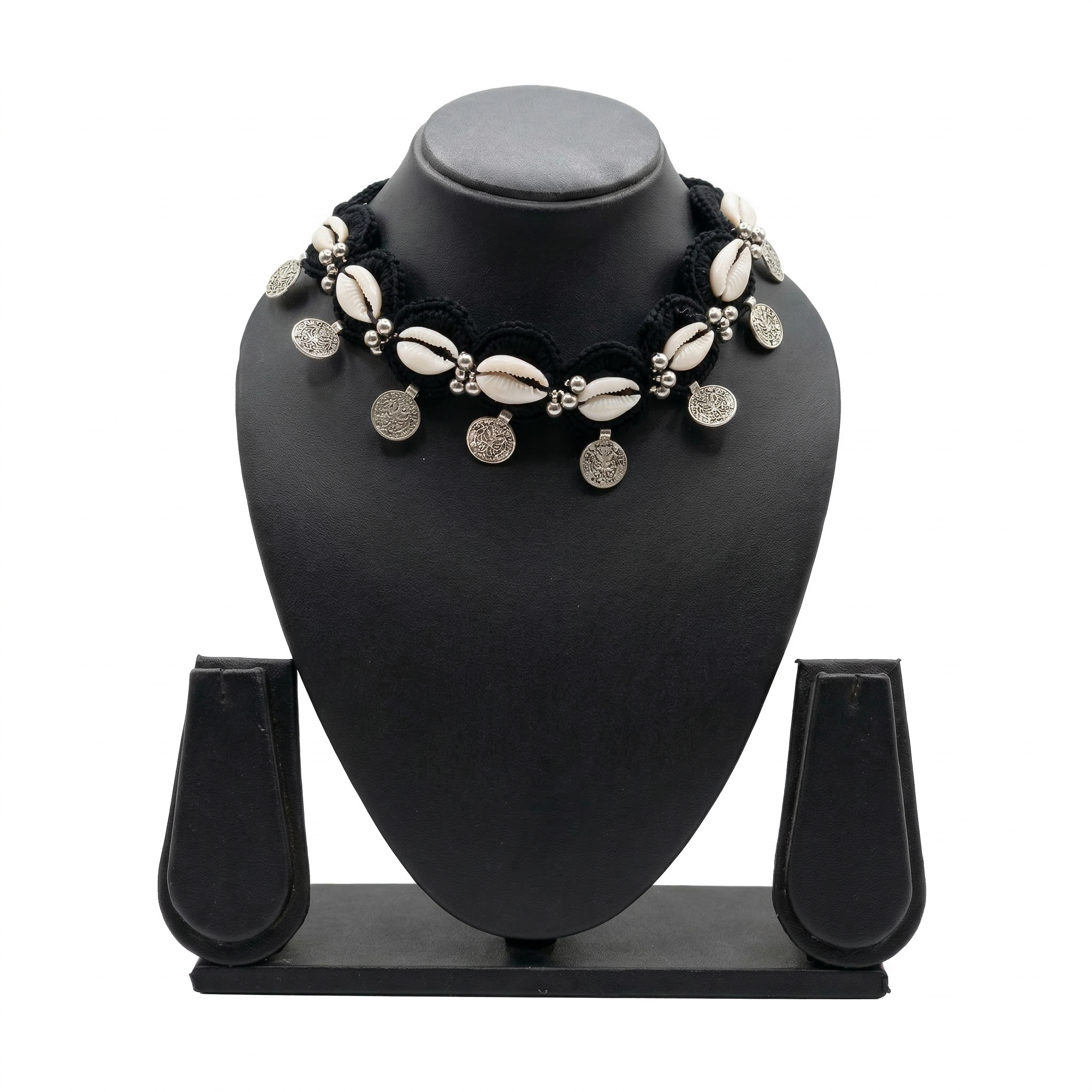 Handmade black crochet choker necklace featuring white cowrie shells and hanging silver bohemian coins on a black display stand.