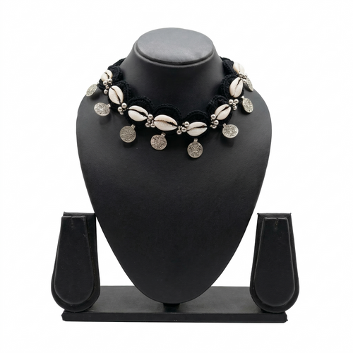Handmade black crochet choker necklace featuring white cowrie shells and hanging silver bohemian coins on a black display stand.
