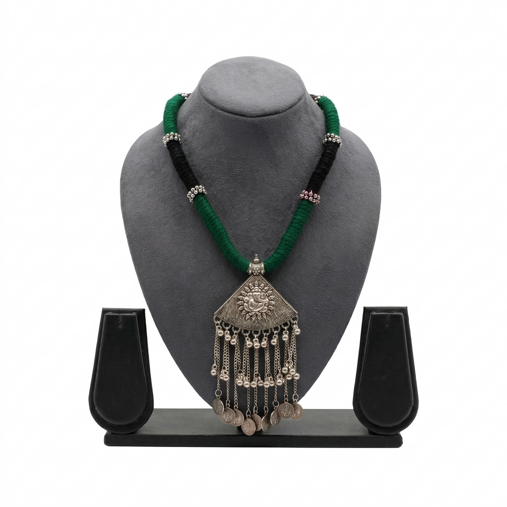 Oxidized silver-tone necklace with a Lord Ganesha pendant, hanging chain tassels, and vintage coin charms on a thick green and black thread cord.