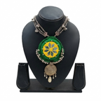 Green fabric mandala necklace with yellow mirror work and oxidized silver charms on a black display stand.