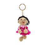 A photorealistic image of a white textured leather tote bag with tan handles and gold hardware. A unique, hand-crocheted amigurumi keychain of a dark-haired girl doll in a pink and magenta dress is attached to the bag, set against a seamless white studio background.