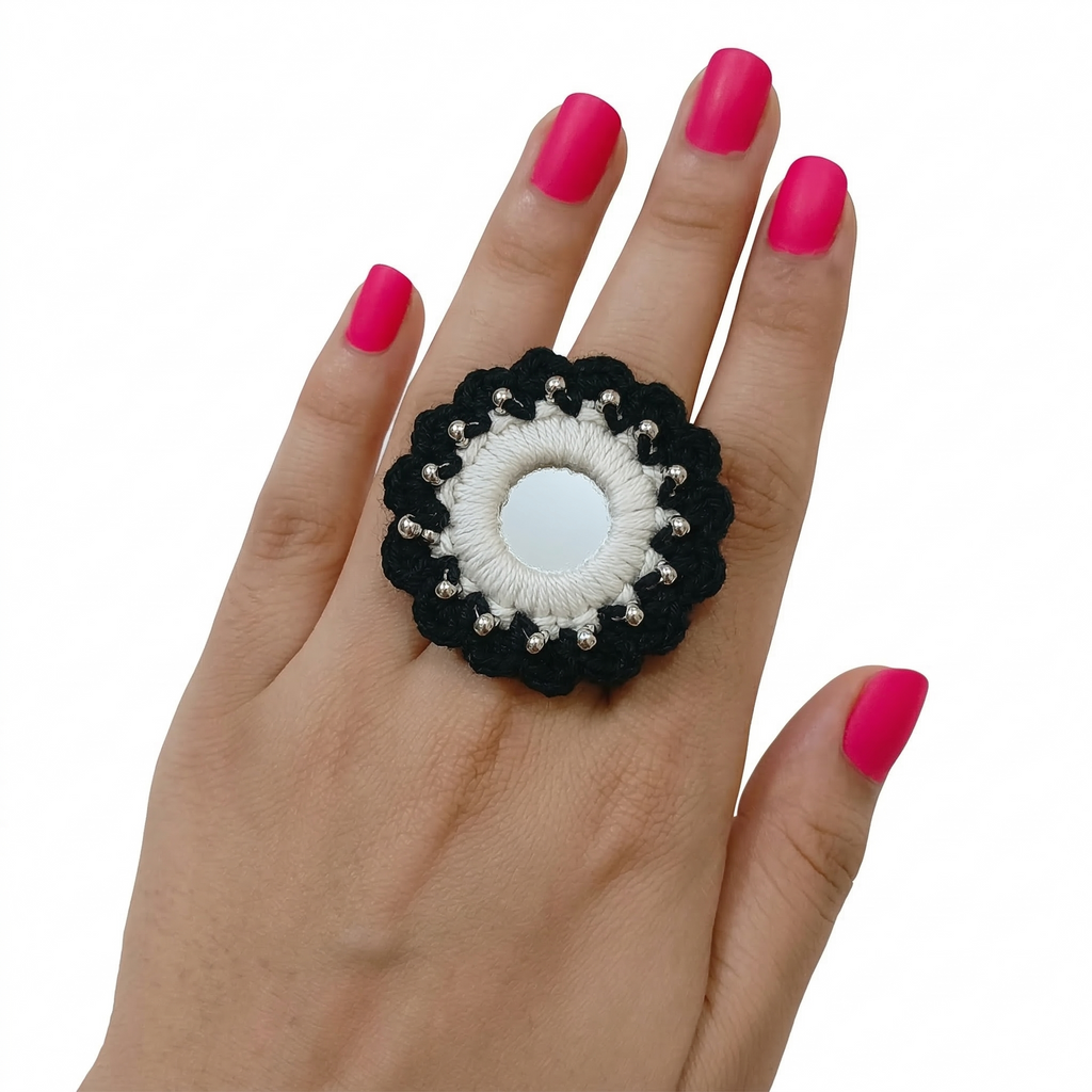 Adjustable handmade black and white crochet finger ring featuring a central round mirror and silver bead detailing on a model's hand.