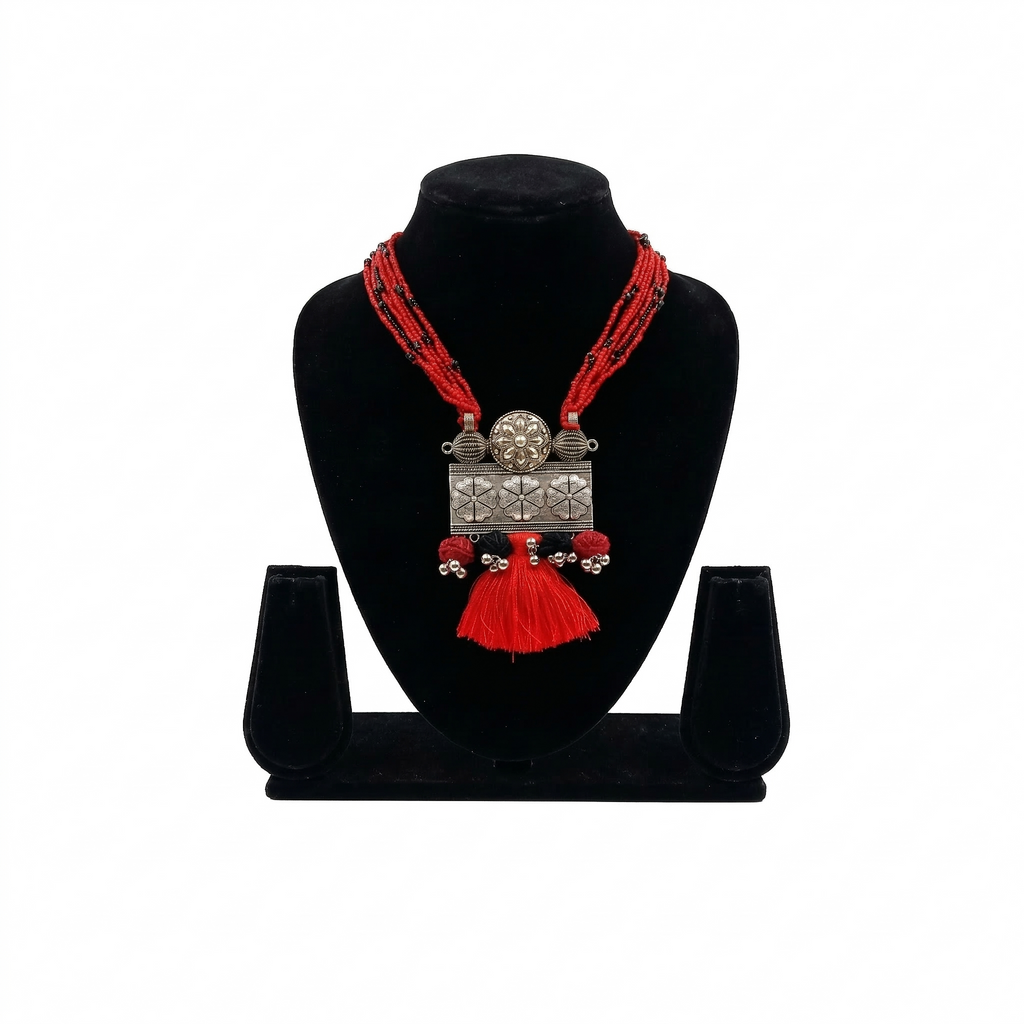 Oxidized silver floral pendant necklace with multiple rows of red seed beads and a red tassel, displayed on a black jewelry bust against a white background.