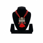 Oxidized silver floral pendant necklace with multiple rows of red seed beads and a red tassel, displayed on a black jewelry bust against a white background.