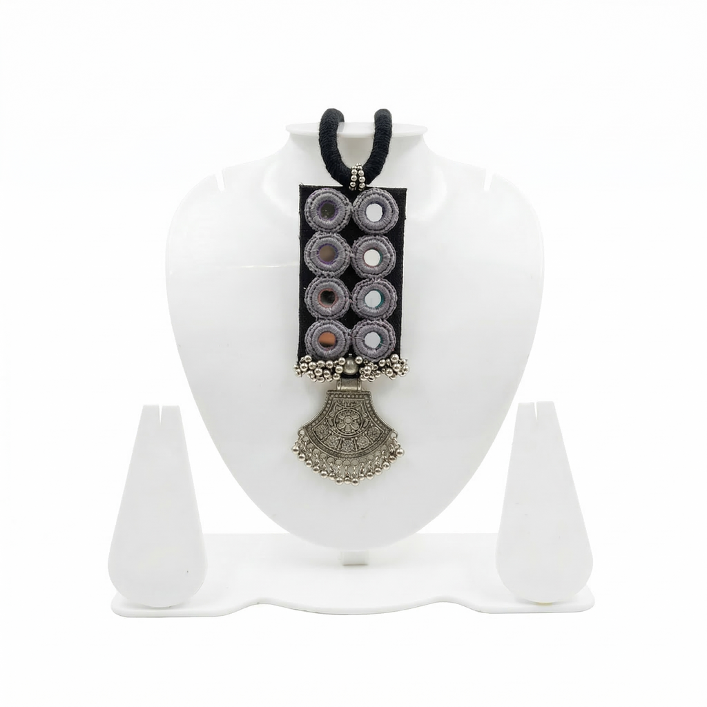 Handmade black fabric choker necklace featuring traditional mirror work embroidery and a vintage-style oxidized silver pendant on a white jewelry display stand.