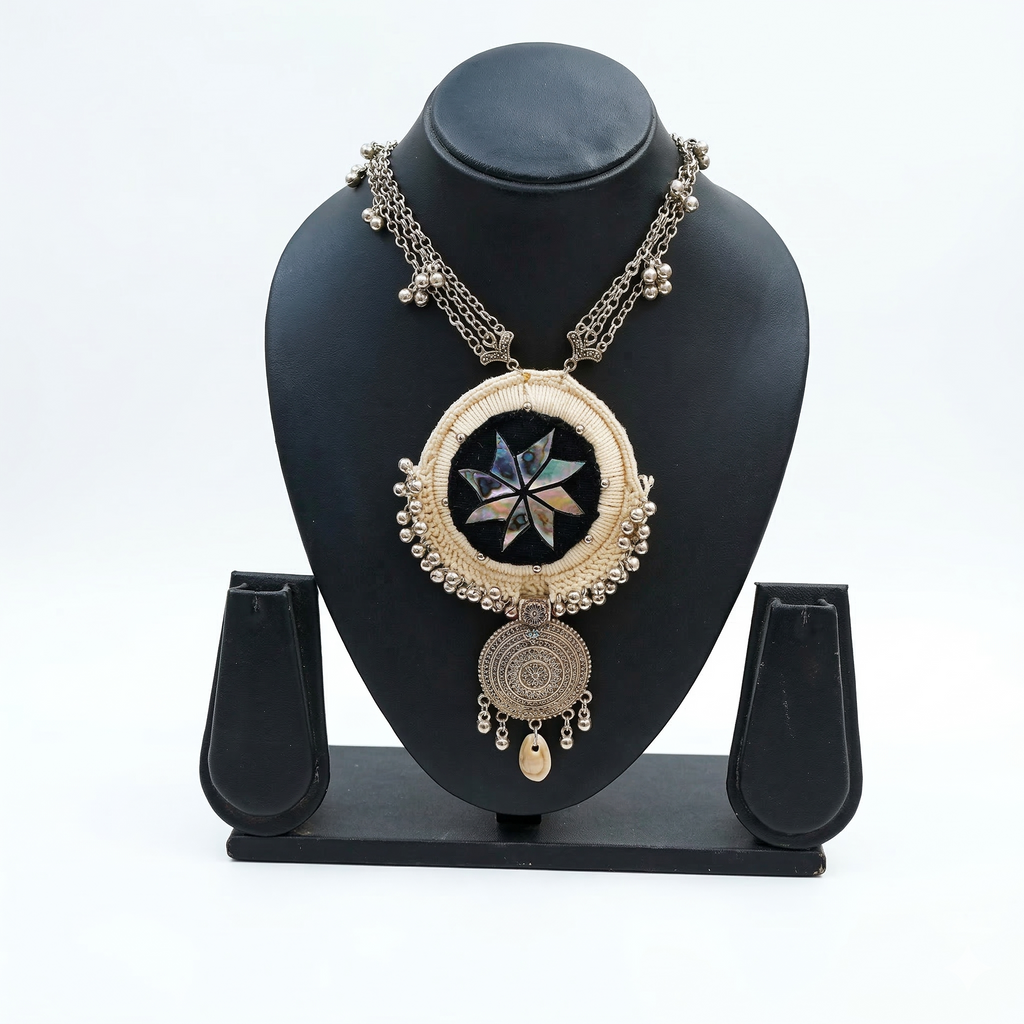 Oxidized silver ethnic necklace featuring a circular cream thread-wrapped pendant with central star mirror work on a black mannequin.