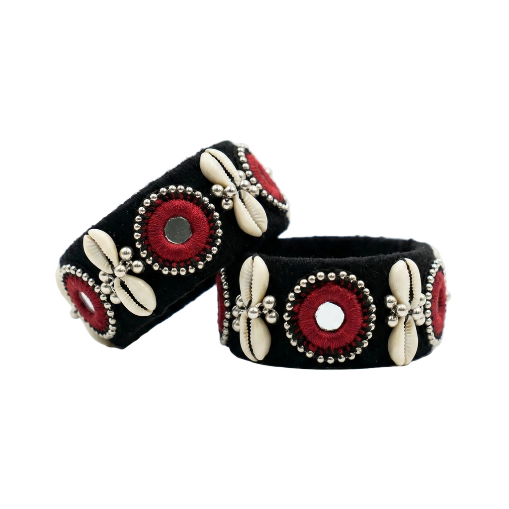 Pair of black velvet ethnic bangles featuring red embroidery, small mirrors, and white cowrie shell accents on a plain white background.
