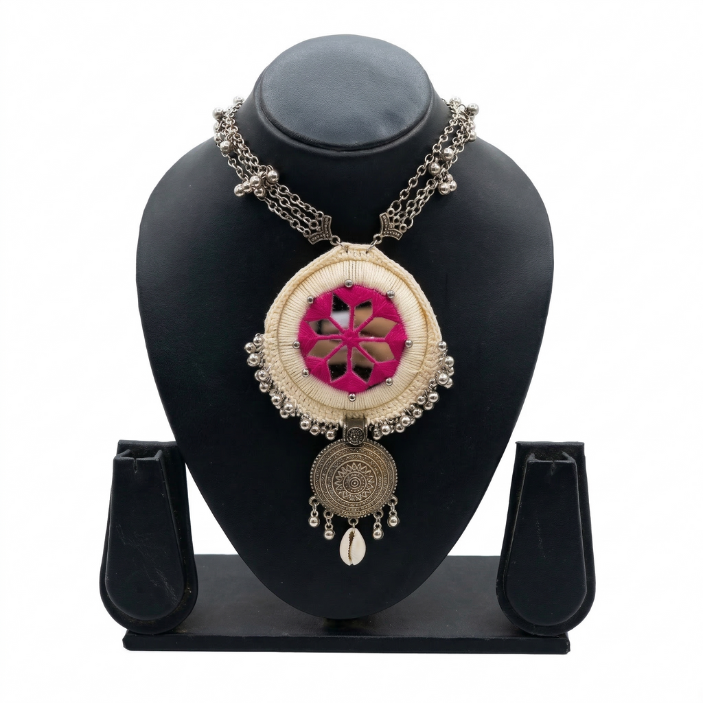 Tribal style handcrafted necklace with pink mirror embroidery and silver charms on a black jewelry bust display.