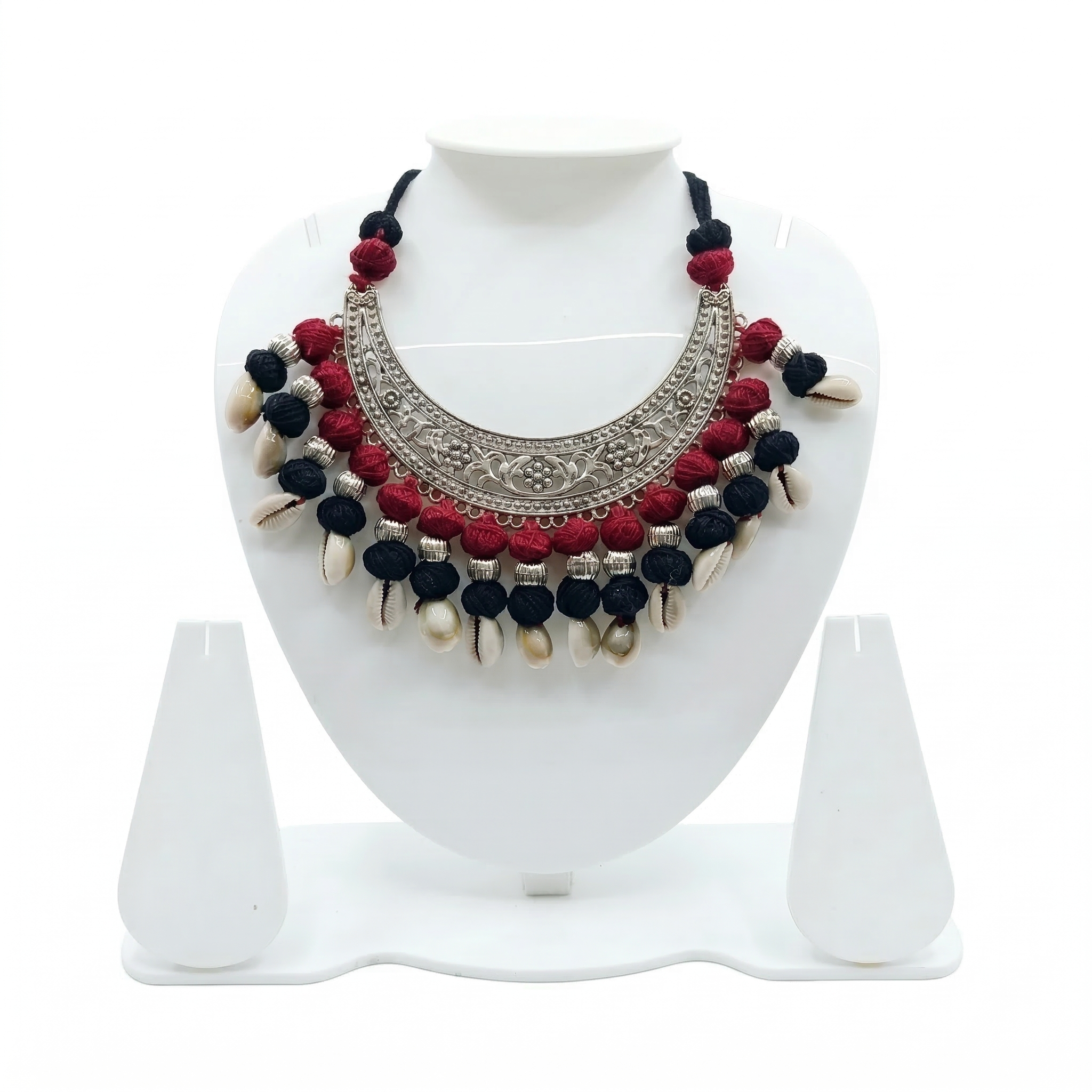 Tribal style oxidized silver crescent choker necklace featuring red and black thread beads and hanging cowrie shells on a white display stand.