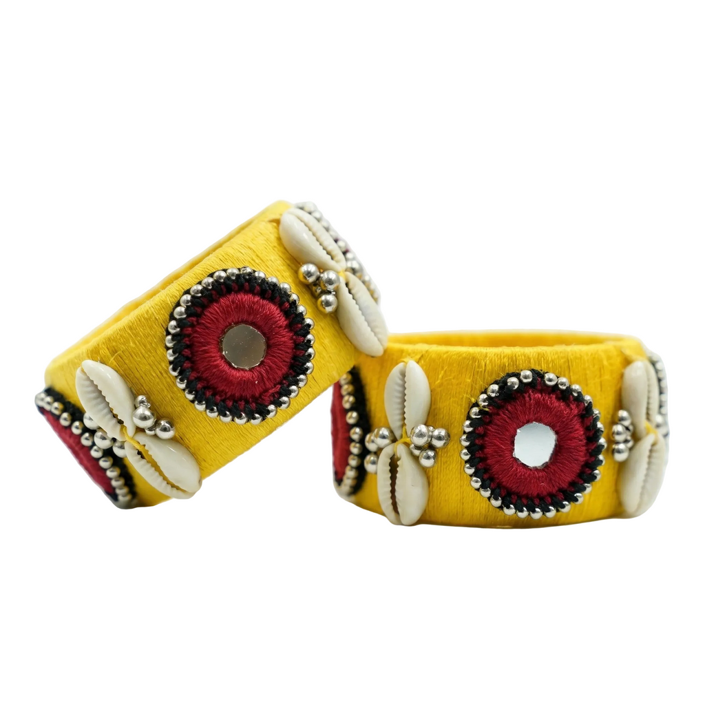 Pair of yellow silk thread wrapped ethnic bangles featuring maroon mirror work borders and white cowrie shell embellishments on a plain white background.