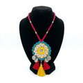 Traditional Indian handmade crochet pendant necklace featuring white cowrie shells, silver coins, and vibrant red and yellow tassels on a black display stand.