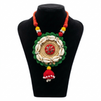 Handmade ethnic jute necklace featuring white cowrie shells, green crochet border, red mirror-work center, and hanging tassel on a black display stand.