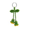 image of a handmade green and yellow crochet flower keychain with two bell-shaped blossoms and leaves on a plain white background.
