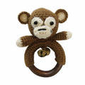 Hand-crocheted brown monkey baby rattle toy with a natural wood teething ring and brass bell on a white background.