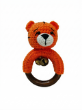 Orange crochet tiger baby rattle with a wooden teething ring and small brass bells on a white background.