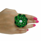 Vibrant green and black crochet flower ring featuring a central mirror and silver bead accents on a person's hand.