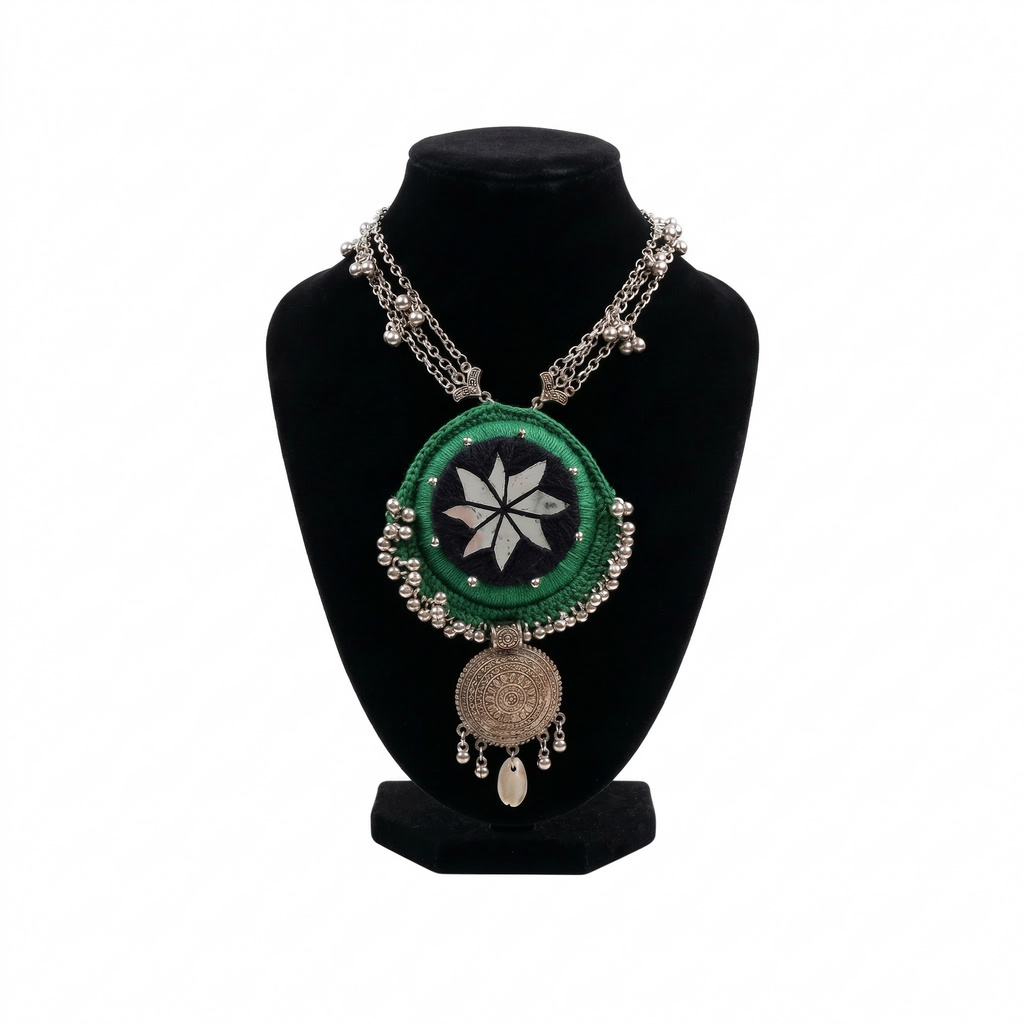Traditional Indian-style green crochet pendant necklace with mirror work and silver bead trim on a black display stand.
