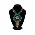 Traditional Indian-style green crochet pendant necklace with mirror work and silver bead trim on a black display stand.