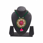 Handmade green and pink tribal necklace with cowrie shells on a black jewelry display stand.