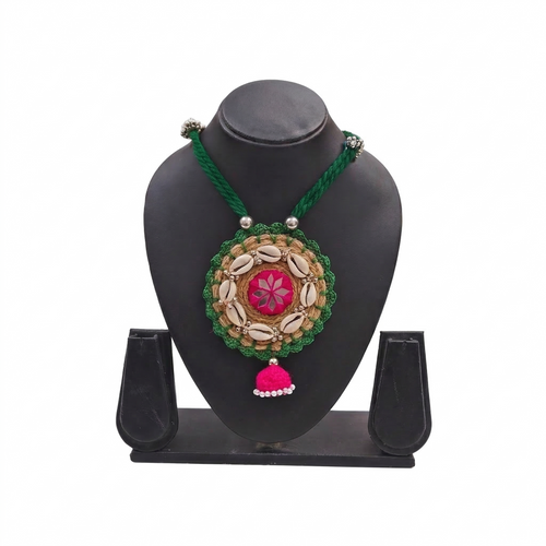Handmade green and pink tribal necklace with cowrie shells on a black jewelry display stand.