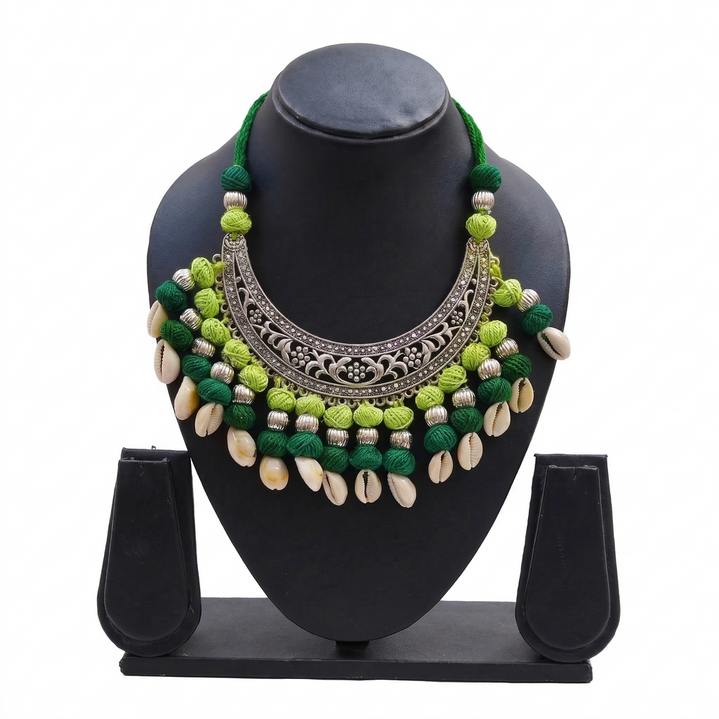 Green handcrafted thread choker necklace with oxidised silver floral crescent and hanging cowrie shells on a black display stand.