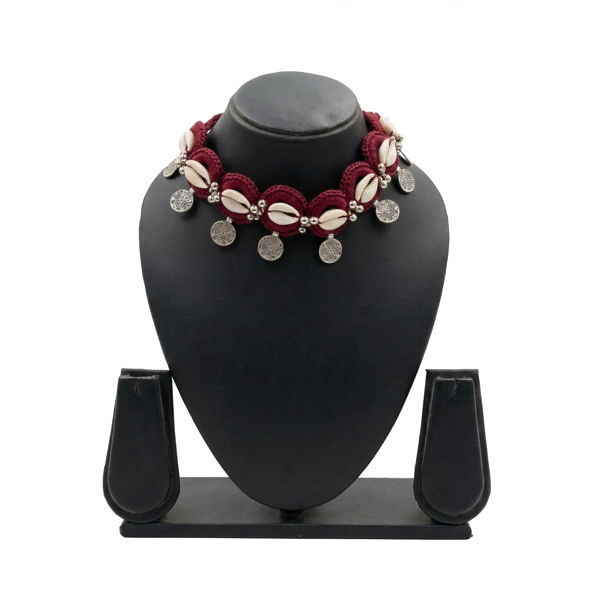 Handmade maroon crochet choker necklace featuring white cowrie shells and hanging silver bohemian coin charms on a black display stand.