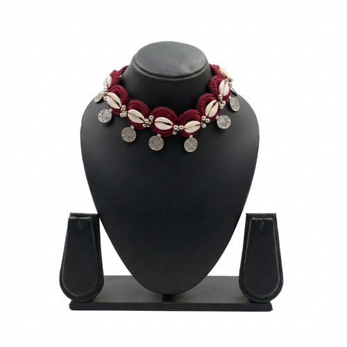Handmade maroon crochet choker necklace featuring white cowrie shells and hanging silver bohemian coin charms on a black display stand.