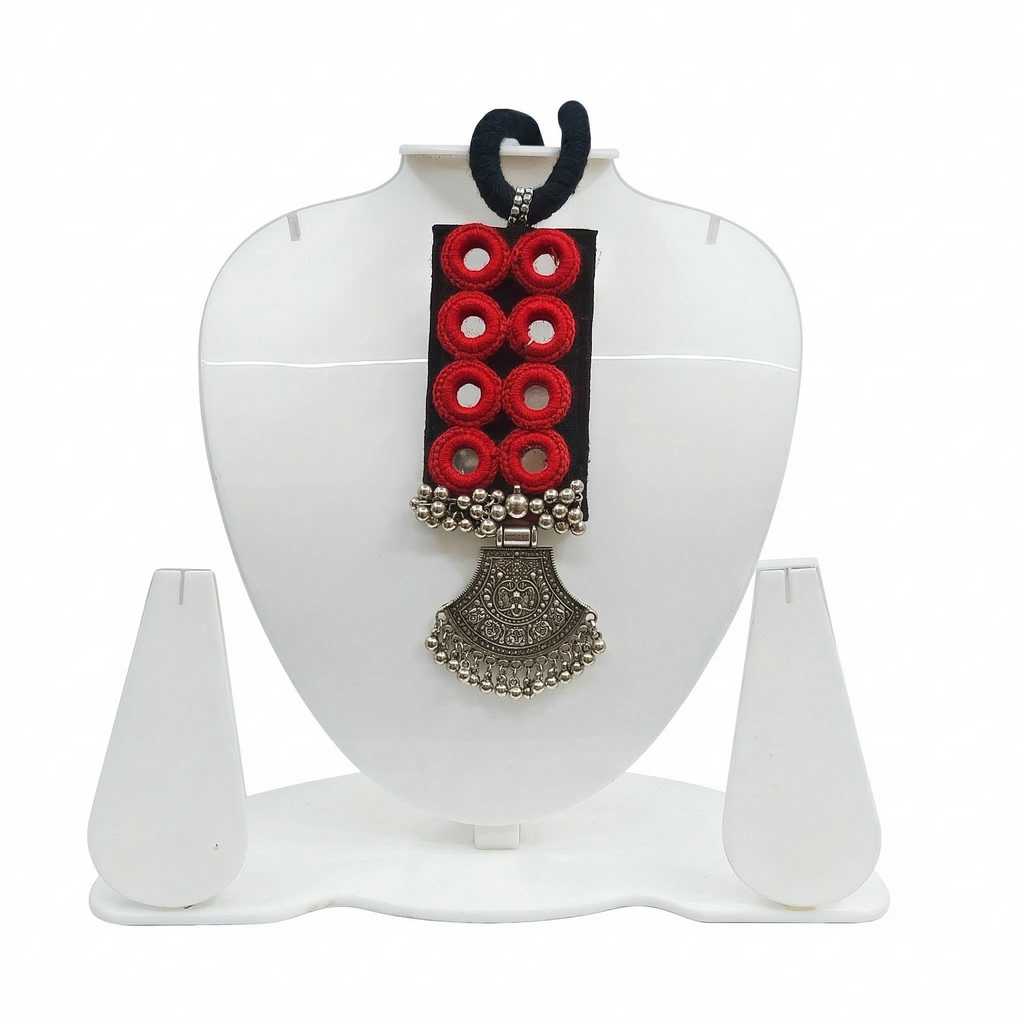 Handmade black fabric necklace featuring eight red-bordered mirrors and a large oxidized silver traditional tribal pendant on a white display stand.