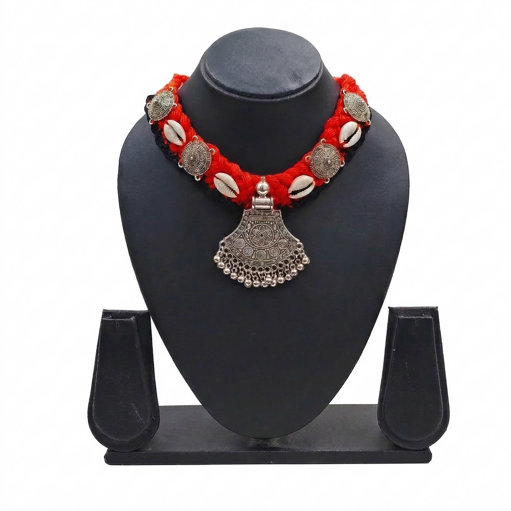 Traditional Indian oxidized silver pendant necklace on a red braided thread with cowrie shell accents and tribal metal charms, displayed on a black jewelry bust.