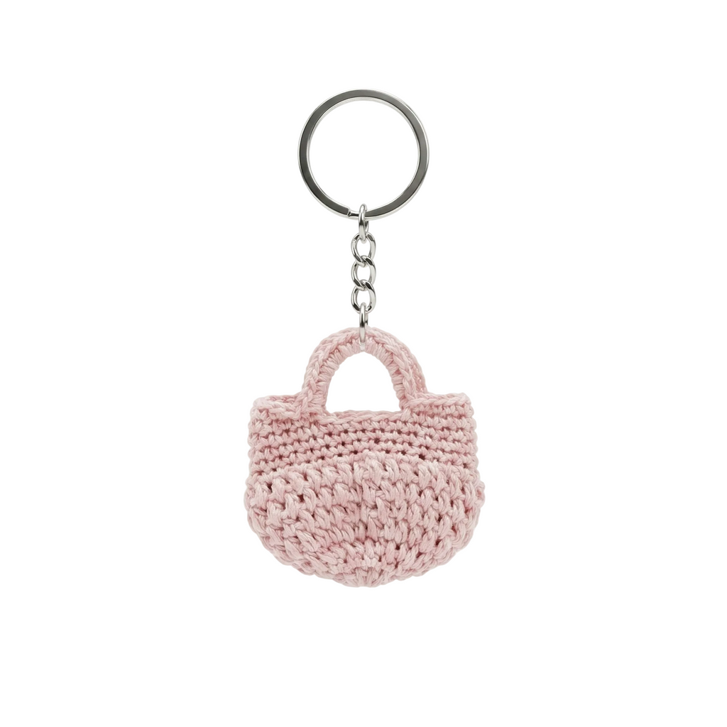 A photorealistic 4K image of a small, dusty pink hand-crocheted mini tote bag keychain on a silver ring, isolated on a white background.