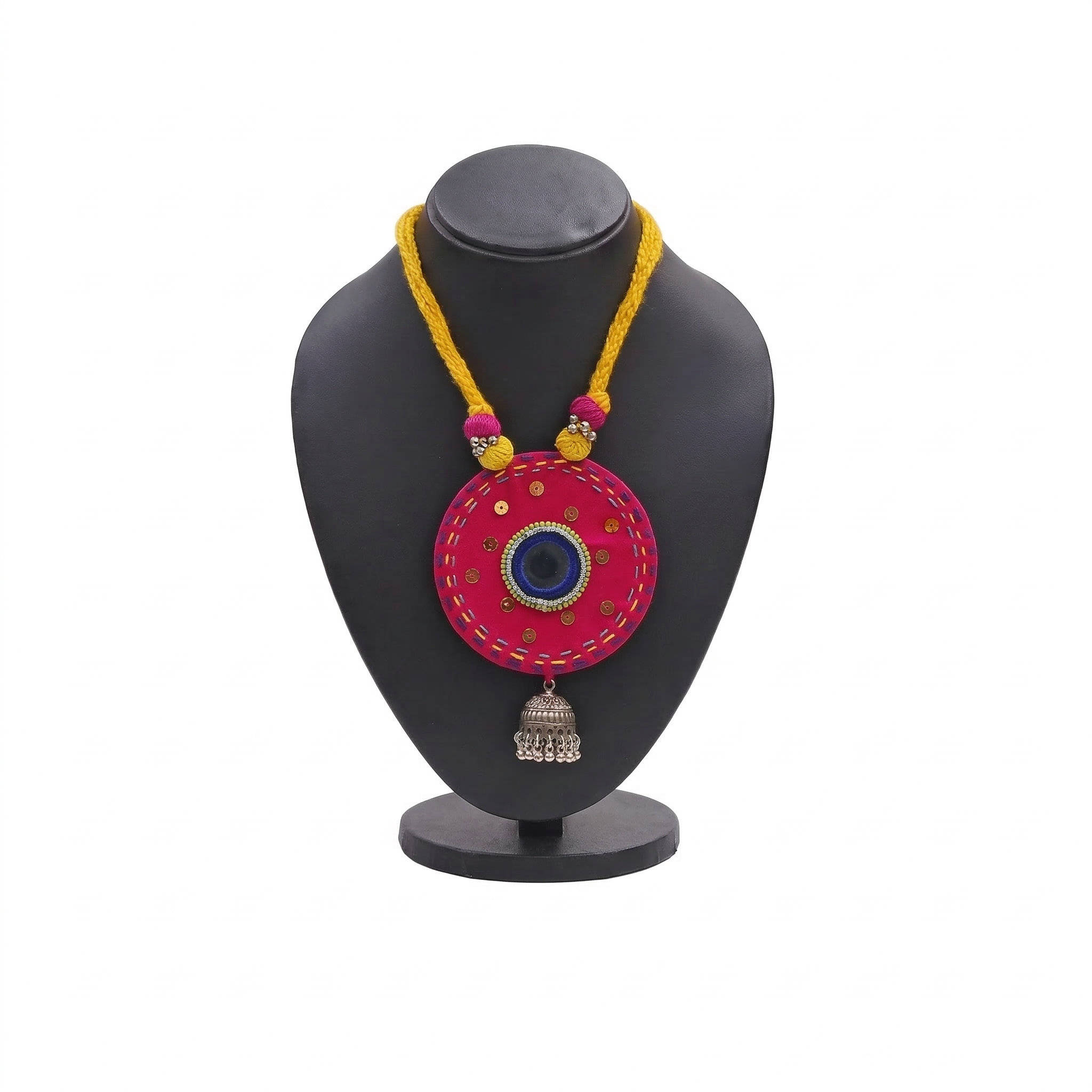 Pink fabric medallion necklace with mirror work, yellow braided cord, and silver jhumka charm on a black display stand.