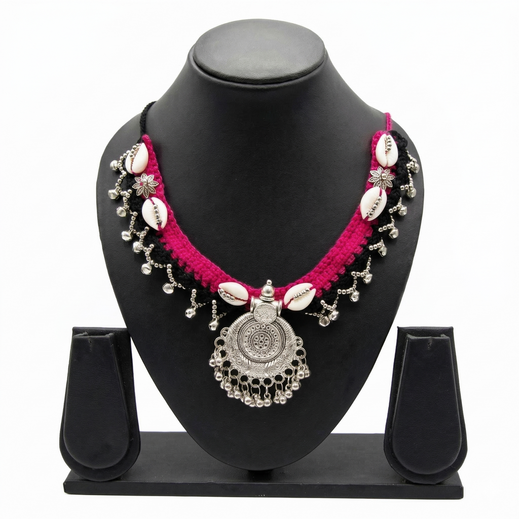Tribal style pink and black crochet necklace with cowrie shells and silver oxidized pendant on a display stand.