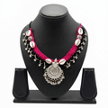 Tribal style pink and black crochet necklace with cowrie shells and silver oxidized pendant on a display stand.