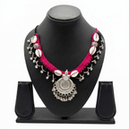 Tribal style pink and black crochet necklace with cowrie shells and silver oxidized pendant on a display stand.