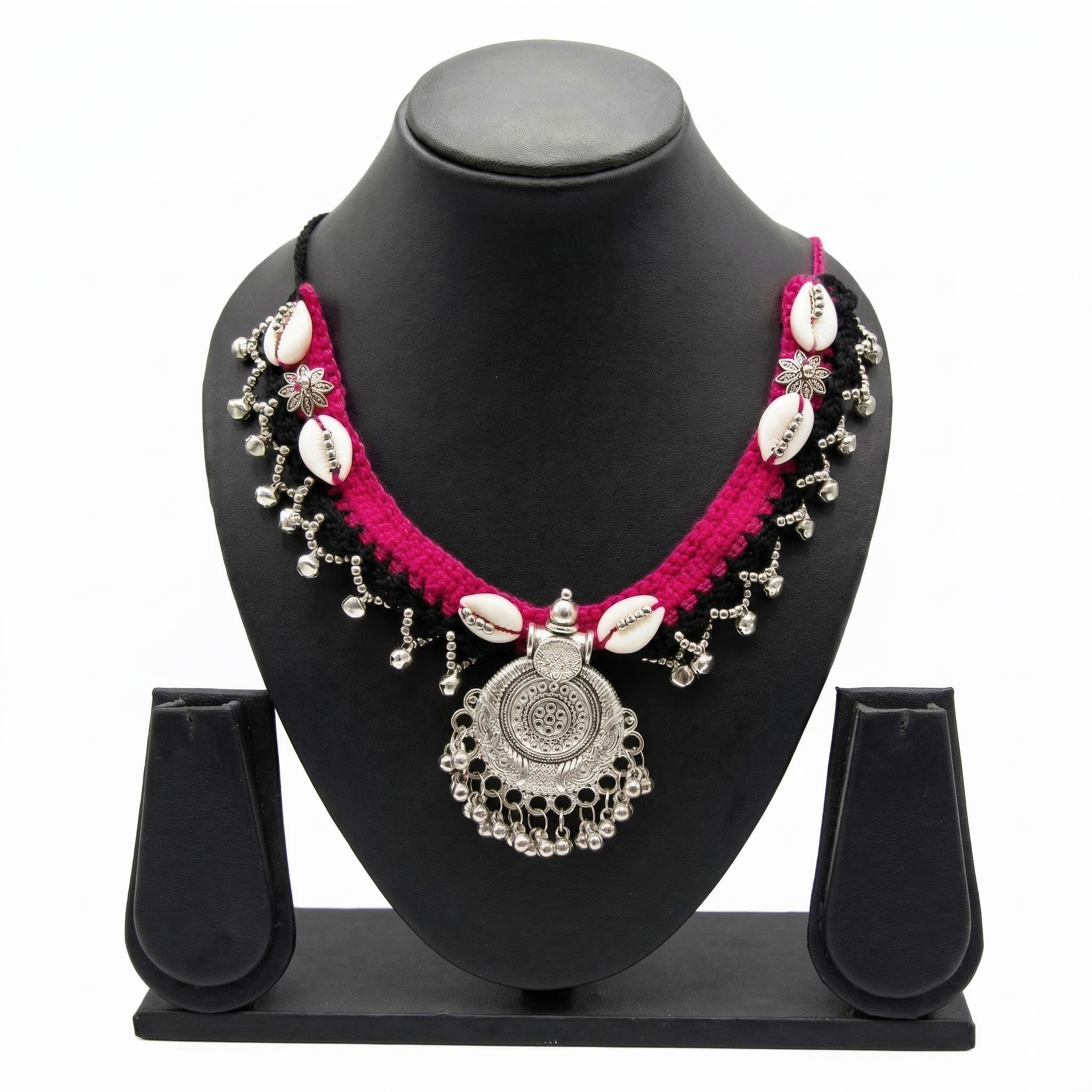 Tribal style pink and black crochet necklace with cowrie shells and silver oxidized pendant on a display stand.
