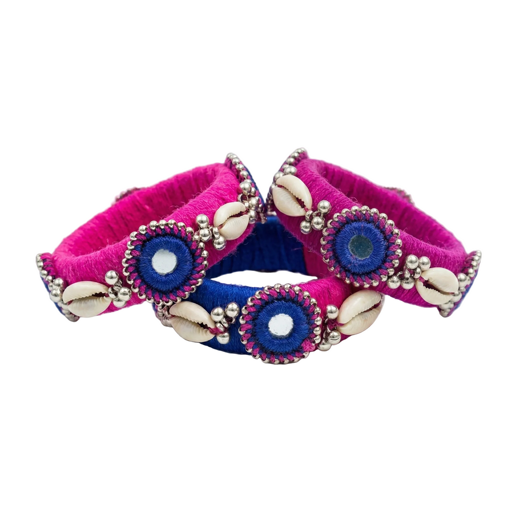 Handmade Pink and Blue Silk Thread Bangles with Cowrie Shells

Alt Text: A set of three vibrant pink and blue silk thread bangles decorated with white cowrie shells, silver beads, and embroidered mirror work on a white background.