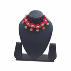 Red crochet choker necklace featuring white cowrie shells and hanging gold coin charms on a black display stand.