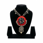 Red fabric choker necklace featuring traditional mirror work and an intricate silver-toned floral pendant on a black display stand.