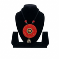 Handcrafted circular red fabric necklace with mirror work detailing and a silver metal jhumka bell pendant on a black bust.