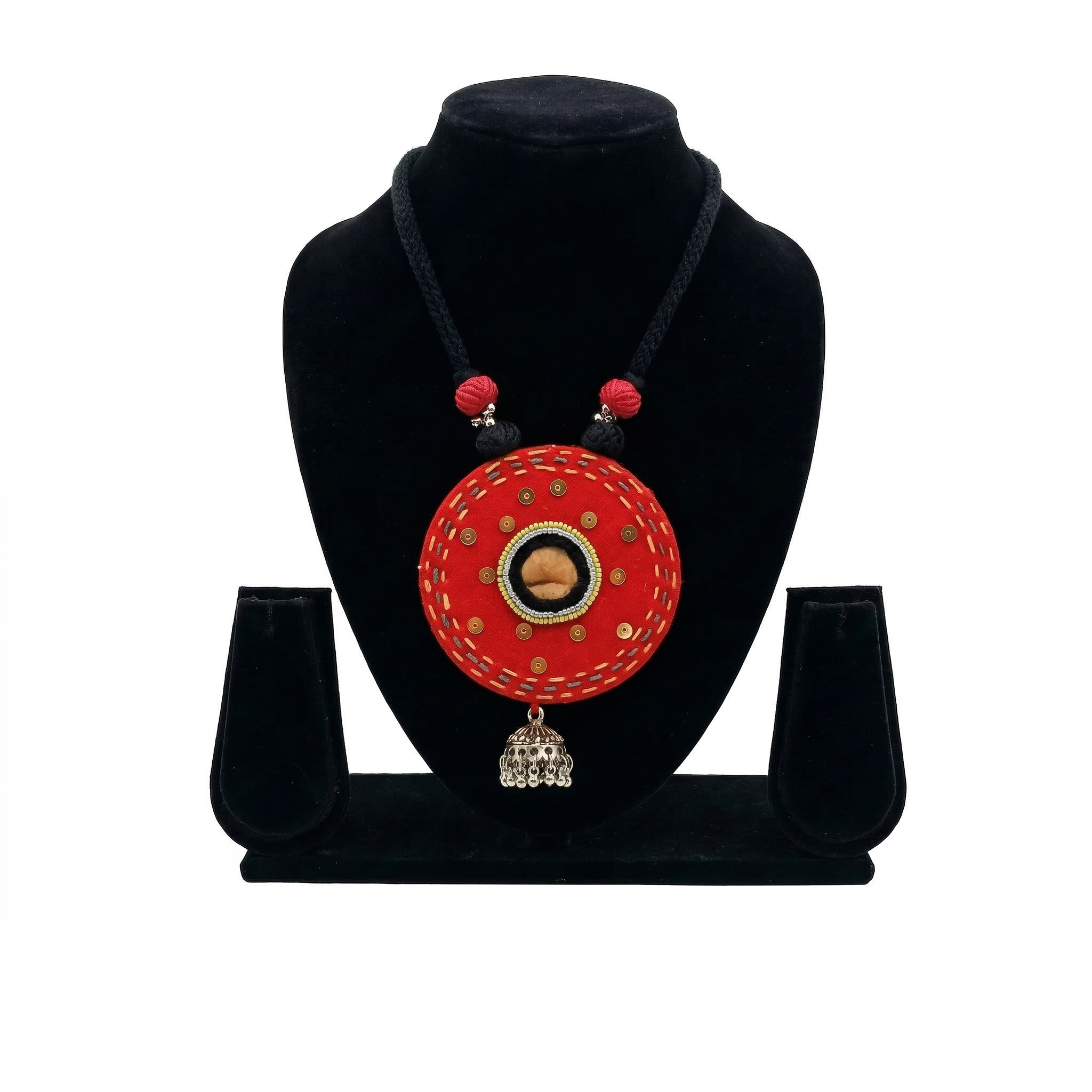 Handcrafted circular red fabric necklace with mirror work detailing and a silver metal jhumka bell pendant on a black bust.