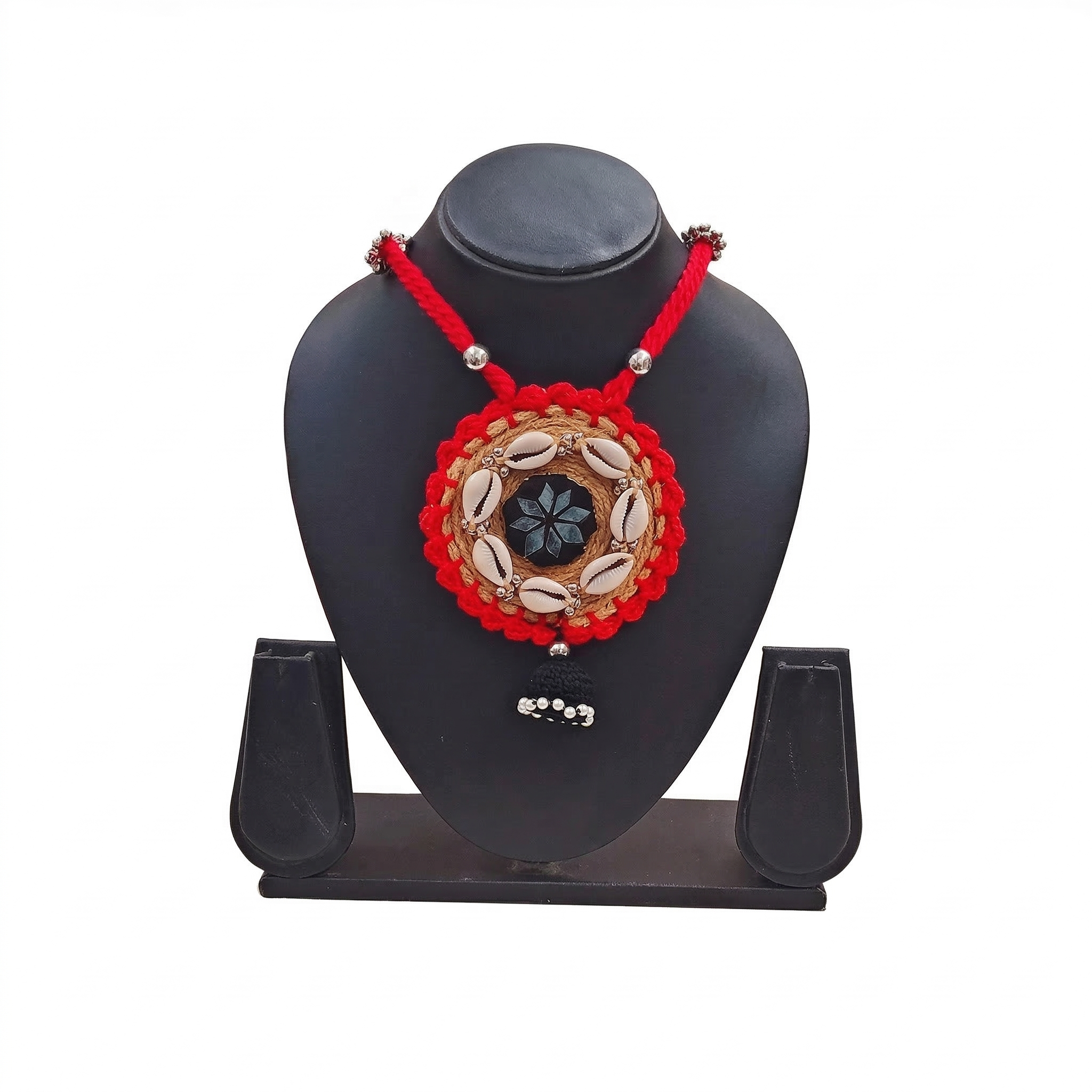 Handmade red and tan jute necklace with cowrie shells and black tassel pendant on a black display stand, white background.