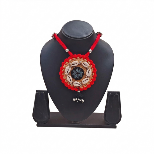 Handmade red and tan jute necklace with cowrie shells and black tassel pendant on a black display stand, white background.