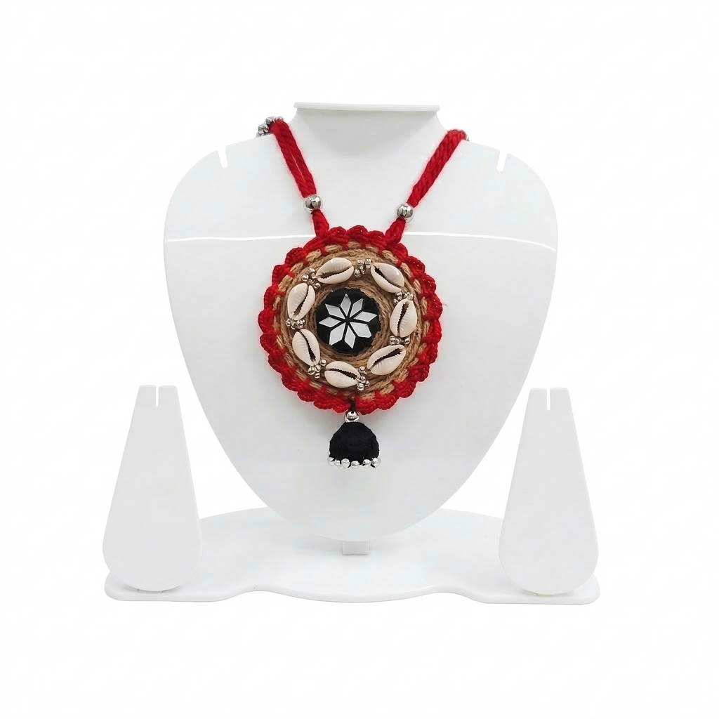 Traditional red handmade necklace on a white display stand featuring jute embroidery, cowrie shells, and a central mirror star design.