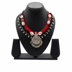 Traditional handcrafted red and black crochet necklace with cowrie shells and oxidized silver pendant on a display stand.