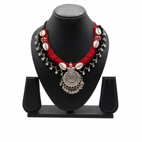 Traditional handcrafted red and black crochet necklace with cowrie shells and oxidized silver pendant on a display stand.