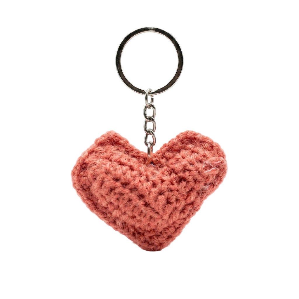 A photorealistic 3D salmon pink crochet heart keychain with a silver metal ring and chain, isolated on a white background.