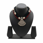 Black and red braided fabric necklace featuring white cowrie shells and a traditional oxidized silver-finish tribal pendant on a black display stand.