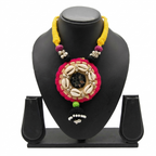 Ethnic handmade necklace with cowrie shells, pink fabric border, and yellow thread cord on a black display stand.