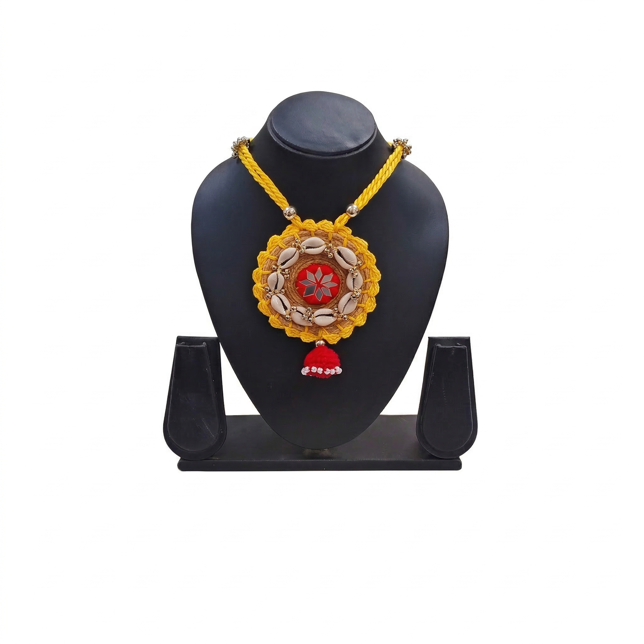 Yellow braided cord necklace featuring a circular pendant with cowrie shells, red mirror work center, and red tassel on a black display stand.